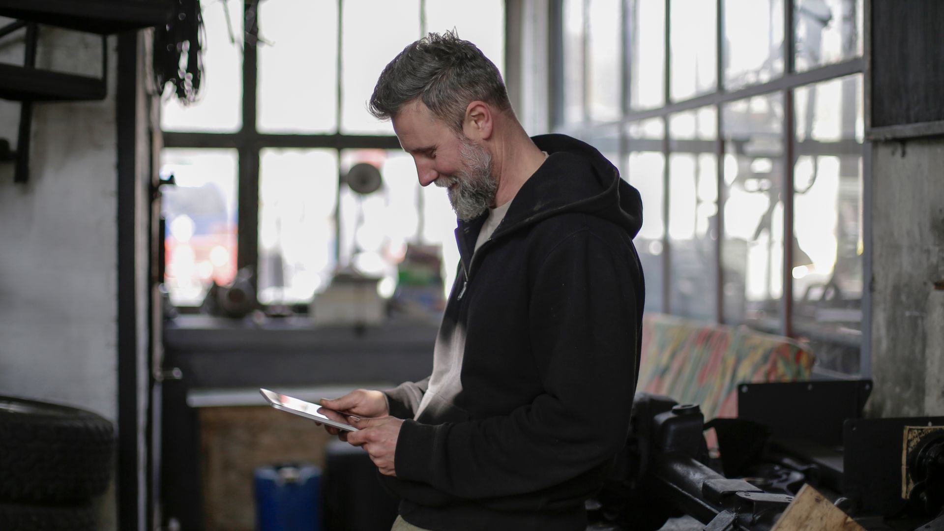 A workshop owner in his fifties reading a tablet at his bench